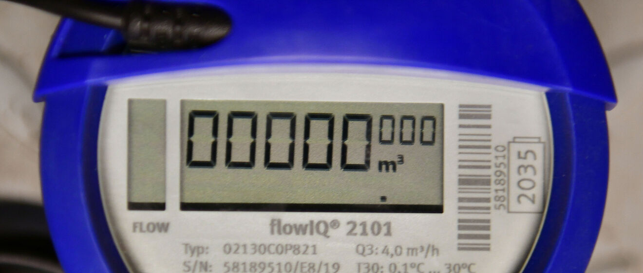 Nahaufnahme eines digitalen Wasserzählers vom Typ flowIQ® 2101 mit blauem Gehäuse. Das Display zeigt den Zählerstand ‚000000 m³‘. Auf dem Gerät sind technische Angaben wie Typ, Seriennummer, Durchflussrate (Q3: 4,0 m³/h), Temperaturbereich (0,1 °C bis 30 °C) sowie Schutzklasse IP68 sichtbar. Ein Kabel ist am oberen Bereich des Zählers angeschlossen. Verlinkung zur Messstellenbetrieb Wasser Seite.