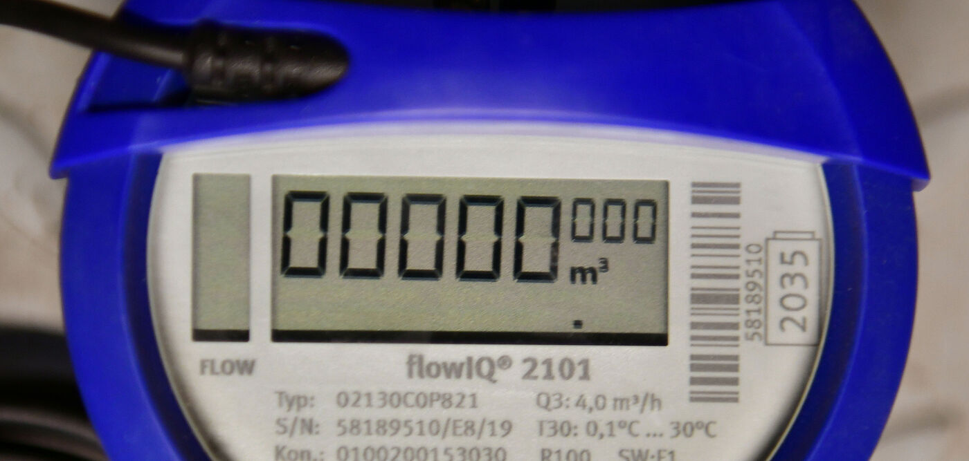 Nahaufnahme eines digitalen Wasserzählers vom Typ flowIQ® 2101 mit blauem Gehäuse. Das Display zeigt den Zählerstand ‚000000 m³‘. Auf dem Gerät sind technische Angaben wie Typ, Seriennummer, Durchflussrate (Q3: 4,0 m³/h), Temperaturbereich (0,1 °C bis 30 °C) sowie Schutzklasse IP68 sichtbar. Ein Kabel ist am oberen Bereich des Zählers angeschlossen. Verlinkung zur Messstellenbetrieb Wasser Seite.