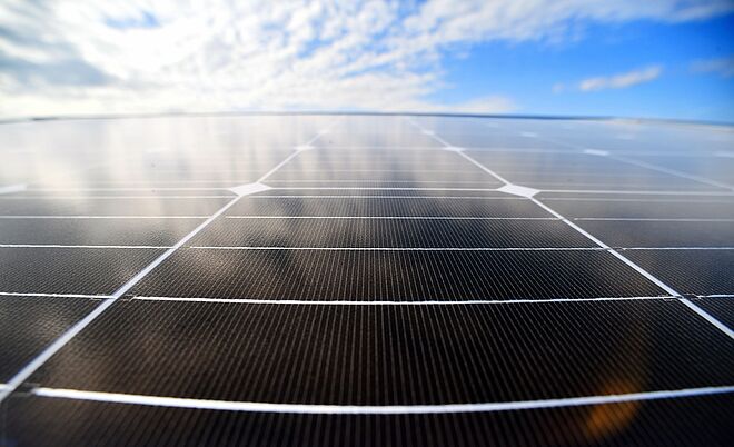 Nahaufnahme einer Photovoltaikanlage unter blauem Himmel mit Wolken: Die glänzende Oberfläche der Solarmodule reflektiert das Licht, die einzelnen Solarzellen sind deutlich erkennbar. Das Bild symbolisiert nachhaltige Energiegewinnung durch Solarstrom und den Einsatz erneuerbarer Energien. Verlinkung zur Einspeisung Seite.