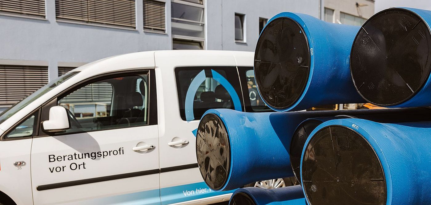 Ein weißer Service‑Transporter der swa Netze GmbH steht vor einem modernen Gebäude. Auf der Fahrzeugseite sind das Logo „swa“ sowie der Schriftzug „Beratungsprofi vor Ort“ gut lesbar. Neben dem Fahrzeug sind mehrere große, blaue Kunststoffrohre mit schwarzen Endkappen auf einem Gestell gestapelt. Die Szene vermittelt einen professionellen Außeneinsatz im Bereich Netze und Infrastruktur.